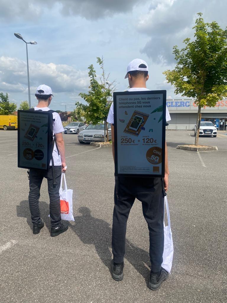 Two promoters walking with backpack screens showing a phone campaign